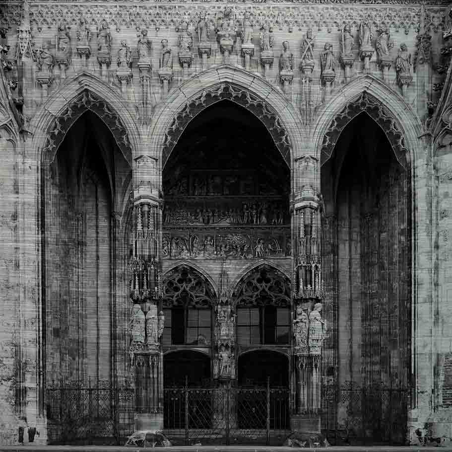 Ulm Münsterportal | Alu Dibond | #1150303 3 - 3 Hauptportal des Ulmer Münsters. Es zeigt das Bild des Hauptportals des Ulmer Münsters mit zwei großen Holztüren und zwei schön verzierte Säulen vor den Holztüren. Im und um das Portal wird mit verschiedenen Figuren und Darstellungen die Erschaffung der Welt erzählt. Das Bild ist in den Farben Schwarz-Weiss.