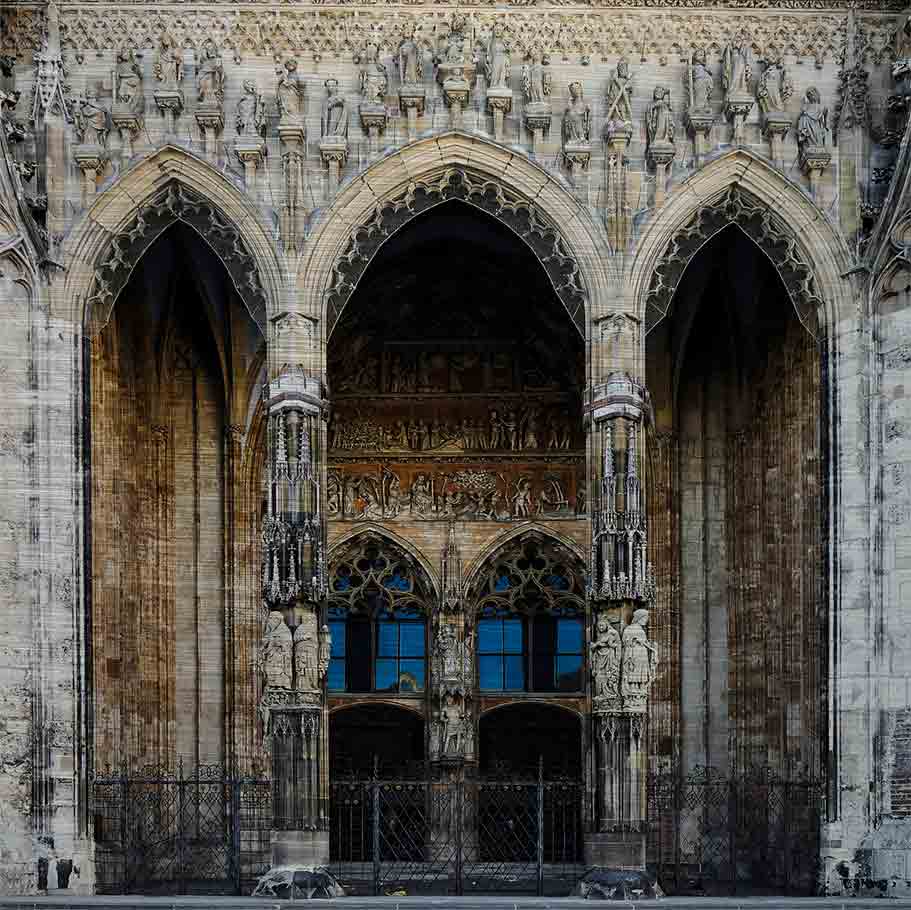 Ulm Münsterportal | Alu Dibond | #1150303-2 3 - 3 Hauptportal des Ulmer Münsters. Es zeigt das Bild des Hauptportals des Ulmer Münsters mit zwei großen Holztüren und zwei schön verzierte Säulen vor den Holztüren. Im und um das Portal wird mit verschiedenen Figuren und Darstellungen die Erschaffung der Welt erzählt. Das Bild ist farbig..
