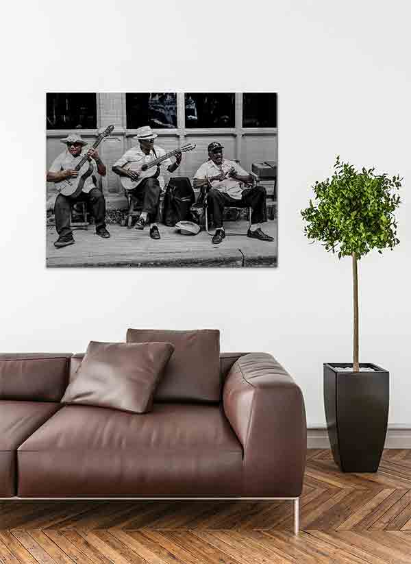 Havanna Musiker | Alu Dibond | #1080058 4 - 4 Havanna Musiker. Es zeigt das Bild von 3 dunkelhäutigen Männern, die vor einem Haus auf dem Gehweg mit ihren Stühlen sitzen und Musik machen. Zwei Männer spielen Gitarre und der andere Mann hat ein kleines Musikinstrument in den Händen. Zwei Männer tragen Hüte und ein Mann eine Baseballmütze. Alle 3 Männer sind adrett gekleidet mit einem weißen Hemd und einer dunklen Anzugshose. Im Hintergrund ist ein Haus mit Holzverkleidung und Fenstern. Das Bild ist in den Farben Schwarz-Weiß kombiniert mit Brauntönen. Das Alu Dibond Bild ist im Querformat und hängt an einer stylischen eingerichteten Wohnzimmerwand.